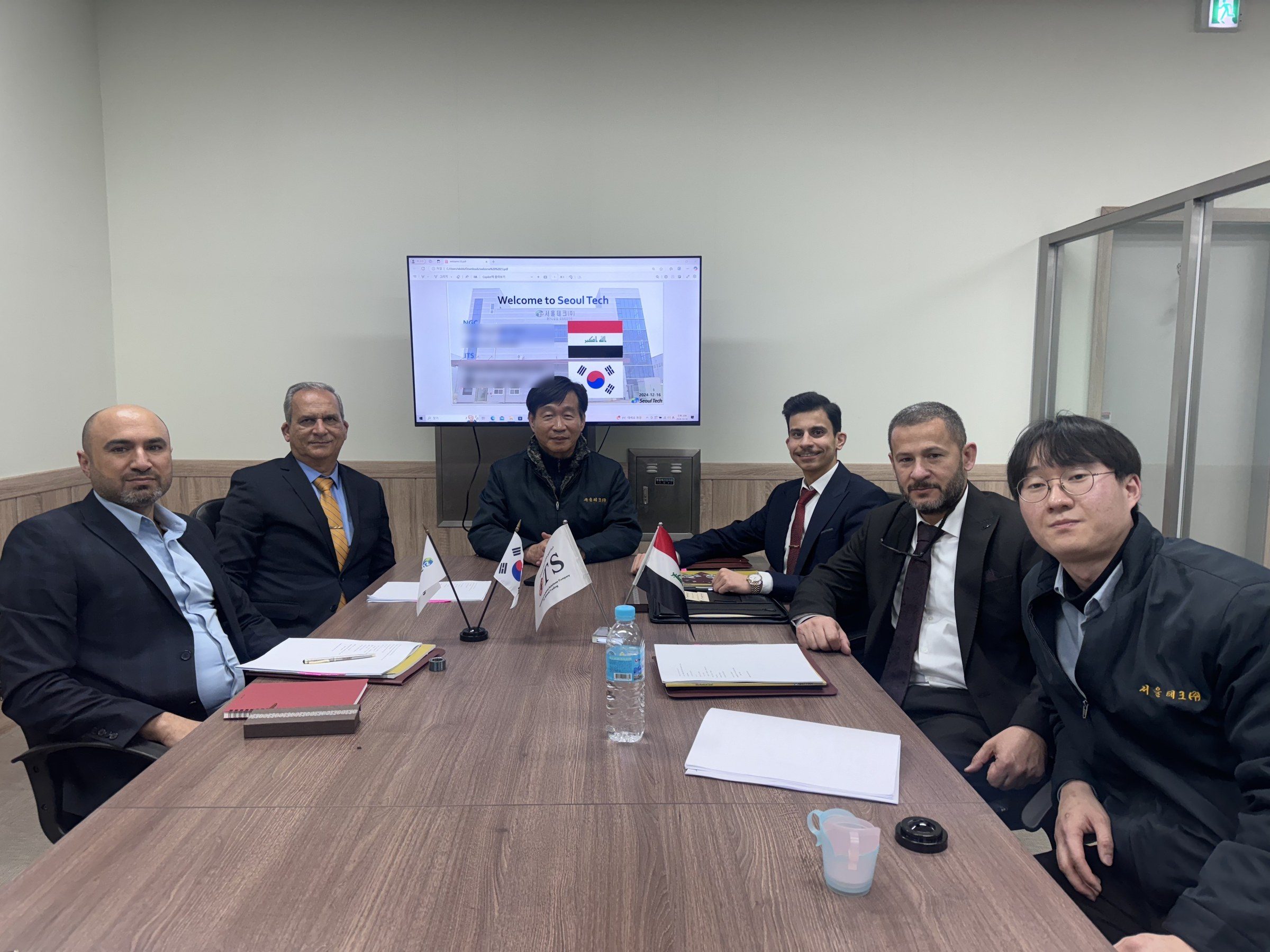 Farooq Mahmood Al Obaidi, Omar Farooq Al Obaidi and an NGC engineer with the Seoul Tech team under a welcome screen.