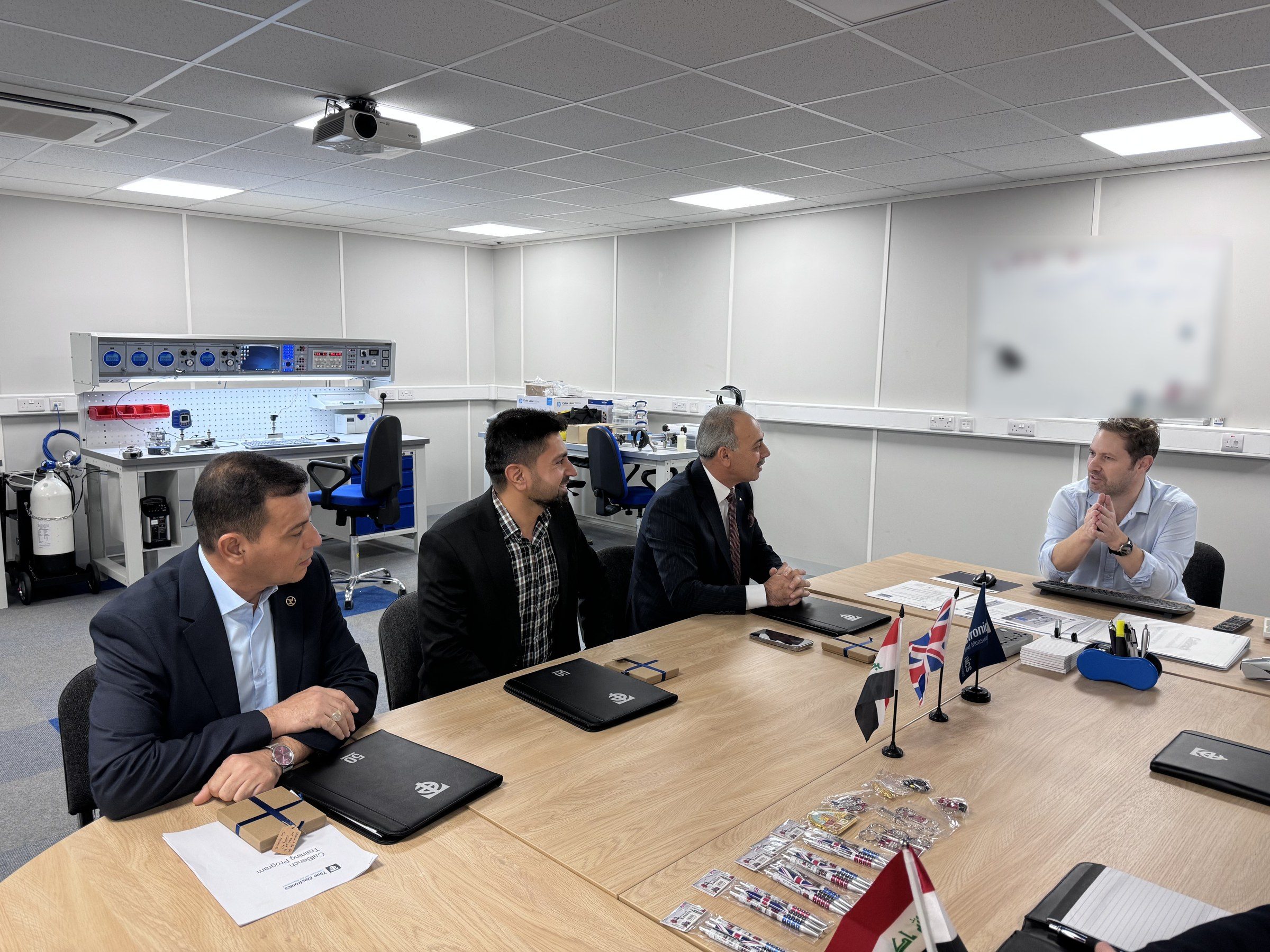 The delegation and Robert Bailey around a meeting table with Iraqi and British desk flags.