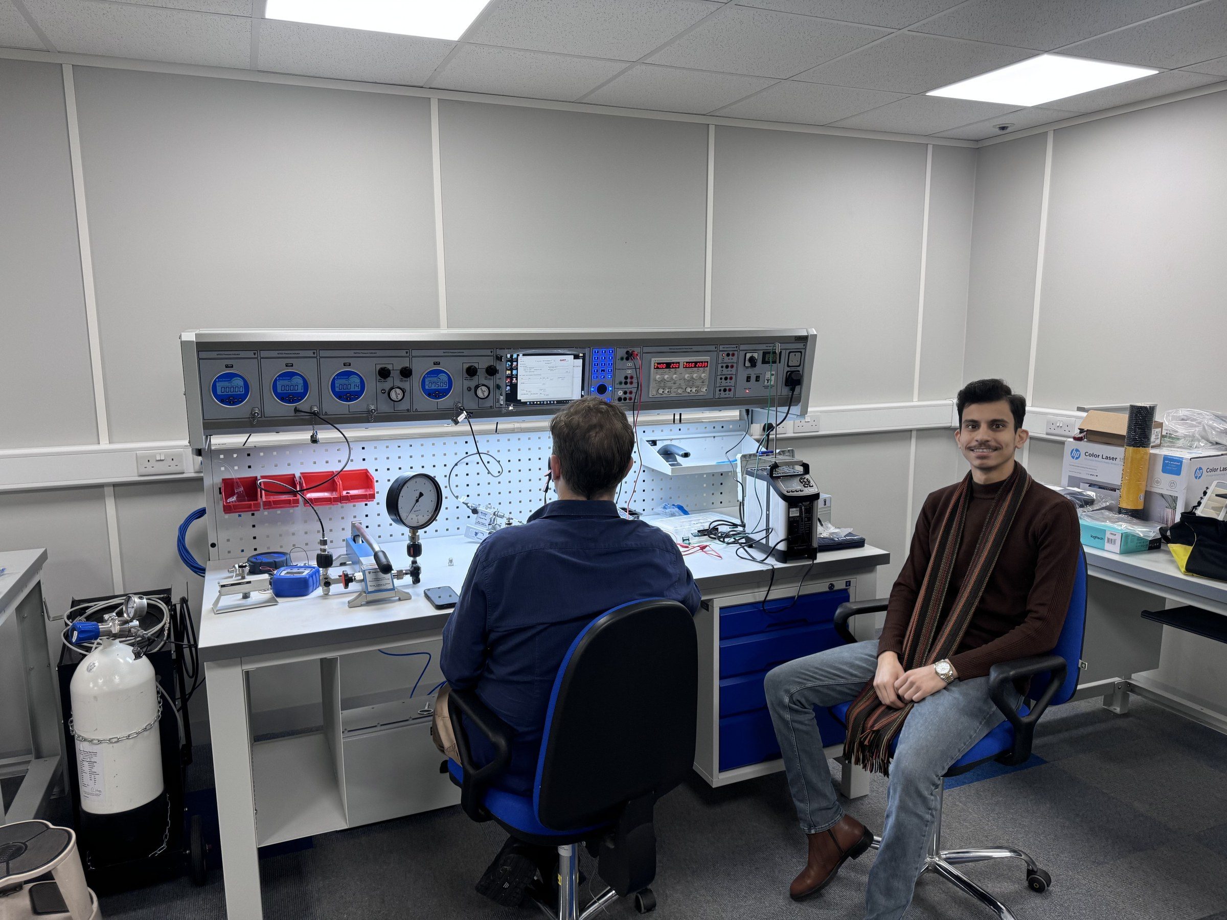 Omar Farooq Al Obaidi seated at the calibration bench beside a Time Electronics engineer.